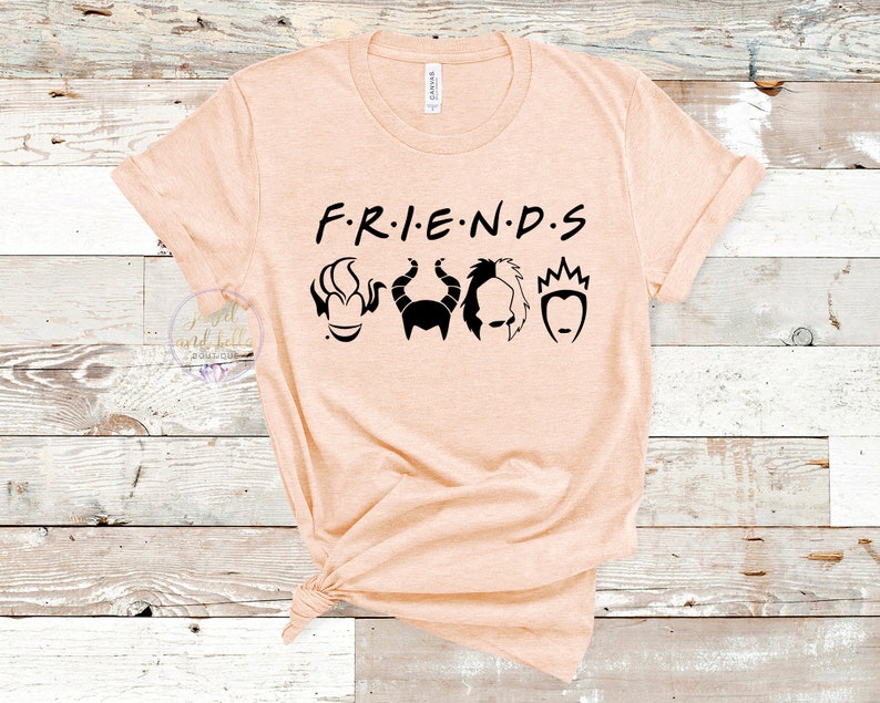 Puede incluir: Una camiseta de color melocot&oacute;n con el texto "F.R.I.E.N.D.S" en negro. Debajo del texto hay cinco siluetas negras de villanos de Disney: &Uacute;rsula, Mal&eacute;fica, Cruella de Vil y la Reina Malvada.