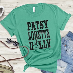 May include: A teal green t-shirt with black text that reads "Patsy Loretta Dolly" with a guitar graphic.