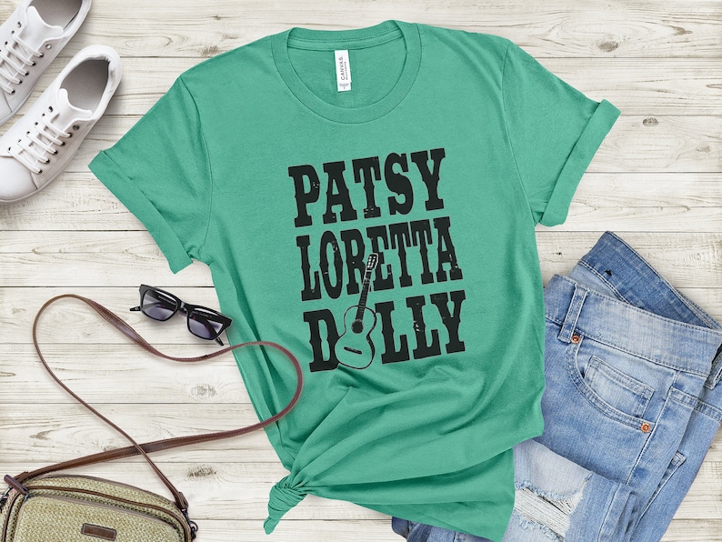 May include: A teal green t-shirt with black text that reads "Patsy Loretta Dolly" with a guitar graphic.