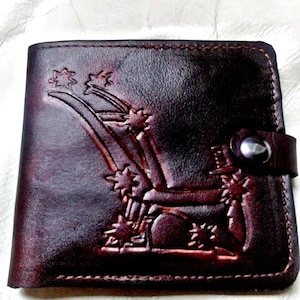 May include: A brown leather wallet with an embossed design of a shooting star. The wallet has a silver snap closure.