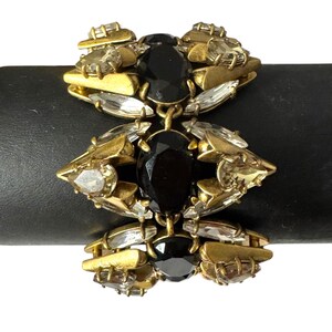 May include: A gold tone bracelet with black and clear faceted stones. The bracelet is made of metal and has a chain link design.