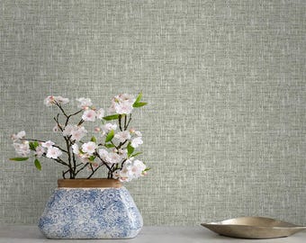 Pode incluir: Um arranjo decorativo com um vaso com padrão azul e branco contendo galhos com flores brancas e rosas. O vaso está sobre uma superfície de mármore branco, com uma tigela dourada à direita. O fundo é uma parede texturizada verde claro.