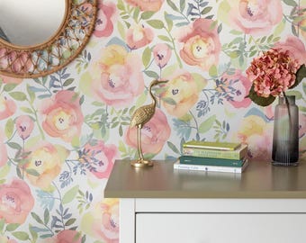 Pode incluir: Papel de parede floral com grandes rosas rosa e amarelas em aquarela e folhas verdes. Uma estátua de grou dourado, livros e um vaso com flores rosa estão em uma cômoda branca com um botão de madeira. Um espelho redondo tecido está pendurado na parede.