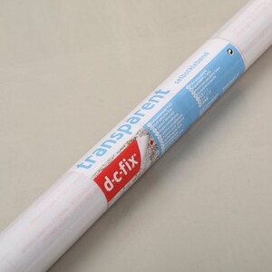May include: A roll of clear, self-adhesive transparent film with the brand name "d-c-fix" and the text "transparent" printed on the label. The label also includes instructions for use and a list of features.