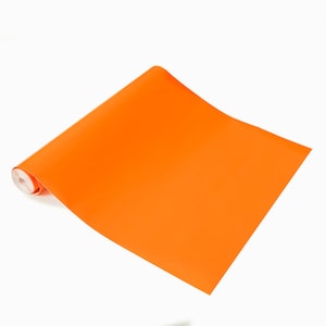 Puede incluir: Un rollo de papel adhesivo de vinilo de color naranja brillante. El papel está enrollado y parcialmente desenrollado, mostrando el color naranja brillante.
