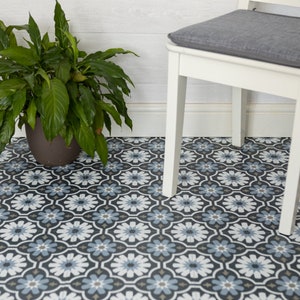 May include: A white chair with a grey cushion sits on a black and white patterned floor. A green plant in a brown pot is in the foreground.