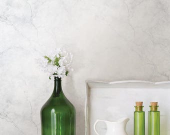 Pode incluir: Uma garrafa de vidro verde com flores brancas, um jarro branco e duas garrafas de vidro verde com rolhas estão sobre uma superfície branca. Uma bandeja branca está atrás do jarro e das garrafas. O fundo é uma parede branca marmoreada.