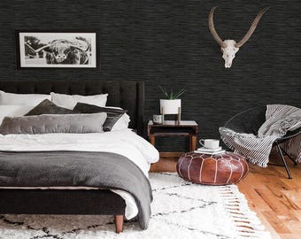 Pode incluir: Um quarto com uma parede texturizada cinza escuro, uma cama com roupa de cama branca e almofadas cinzentas e um tapete branco com um padrão geométrico preto. Uma foto em preto e branco emoldurada e um crânio decorativo adornam a parede.