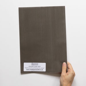 May include: A sample of Quadro Dark Grey woodgrain vinyl wrap. The sample is a dark grey colour with a woodgrain pattern. The text "CREATE YOUR WORLD" and "QUADRO DARK GREY" is printed on the sample. "Thank you for purchasing this sample" is also printed on the sample.