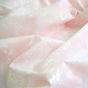 Pode incluir: Tecido rosa claro com um delicado padr&atilde;o floral branco. O tecido &eacute; drapeado, criando dobras e sombras que real&ccedil;am a textura e o design. O padr&atilde;o floral inclui pequenos grupos de pontos e formas de flores maiores.