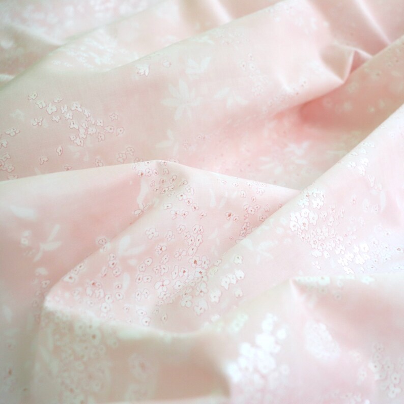 Pode incluir: Tecido rosa claro com um delicado padr&atilde;o floral branco. O tecido &eacute; drapeado, criando dobras e sombras que real&ccedil;am a textura e o design. O padr&atilde;o floral inclui pequenos grupos de pontos e formas de flores maiores.