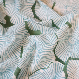 May include: A white fabric featuring a repeating pattern of light blue circular motifs with radiating lines. The design includes dark green organic shapes interspersed between the blue circular patterns, creating a textured and layered visual effect.