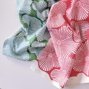 May include: Two pieces of fabric featuring a repeating block-printed floral pattern. One piece displays light blue flowers on a green background, while the other features vibrant pink flowers on a white background, both with radiating petal lines.