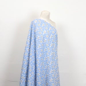 May include: A bolt of fabric draped over a mannequin. The fabric features a pattern of blue and gray shapes on a white background. The fabric is a light, airy material, suitable for clothing or home decor.