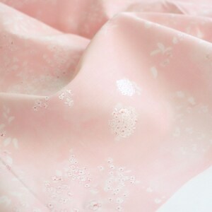 Pode incluir: Close-up de um tecido rosa com um padr&atilde;o floral. O tecido &eacute; macio e fluido, com detalhes florais brancos espalhados pela superf&iacute;cie. O efeito geral &eacute; delicado e feminino, adequado para roupas ou decora&ccedil;&atilde;o de casa.
