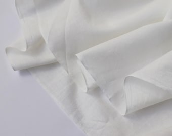 May include: A close-up shot of white fabric with soft folds and subtle textures. The fabric appears to be lightweight, possibly linen or cotton, and drapes gently. The lighting highlights the delicate weave and creates shadows.