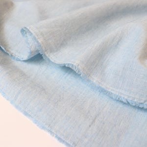 May include: A close-up of a light blue fabric with a raw edge. The fabric has a subtle texture and a soft, airy feel.