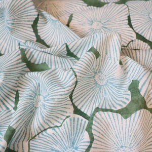 May include: A white fabric featuring a repeating pattern of light blue, radiating, fan-like floral shapes with dark green, organic, leaf-like silhouettes interspersed between the flowers, creating a textured, folded appearance across the surface.