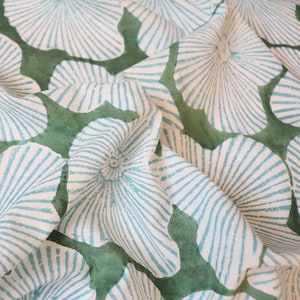 May include: A textile fabric featuring a repeating pattern of light blue, fan-shaped floral motifs with fine radiating lines. The design is set against a solid, muted green background that fills the irregular spaces between the blue flower shapes.