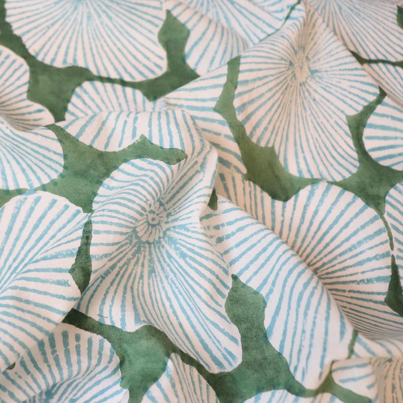 May include: A textile fabric featuring a repeating pattern of light blue, fan-shaped floral motifs with fine radiating lines. The design is set against a solid, muted green background that fills the irregular spaces between the blue flower shapes.
