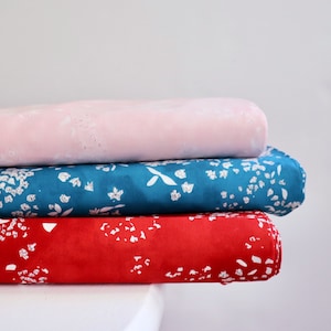 Pode incluir: Tr&ecirc;s rolos de tecido empilhados. O rolo superior &eacute; rosa claro com manchas brancas. O rolo do meio &eacute; azul-petr&oacute;leo com um padr&atilde;o floral branco. O rolo inferior &eacute; vermelho com um padr&atilde;o floral branco.