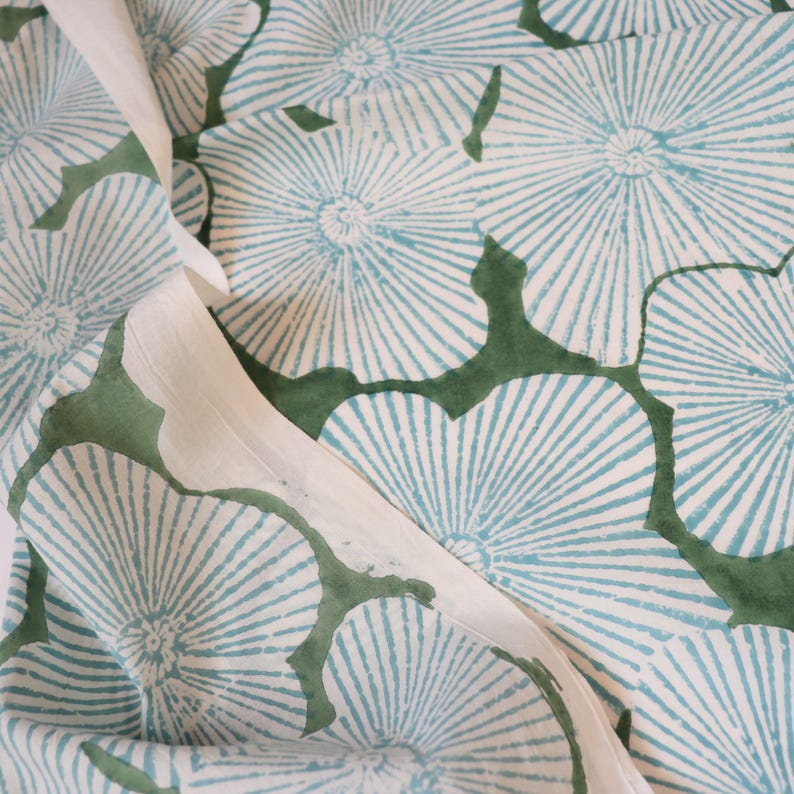 May include: A textile fabric featuring a repeating pattern of light blue, sunburst-style circular floral motifs set against a solid white background, with deep forest green organic shapes filling the negative space between the circular designs.