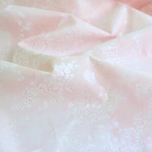 Pode incluir: Tecido rosa claro com um delicado padr&atilde;o floral. O tecido &eacute; drapeado, criando dobras e sombras que real&ccedil;am o design. Pequenos motivos florais brancos est&atilde;o espalhados sobre o fundo rosa.