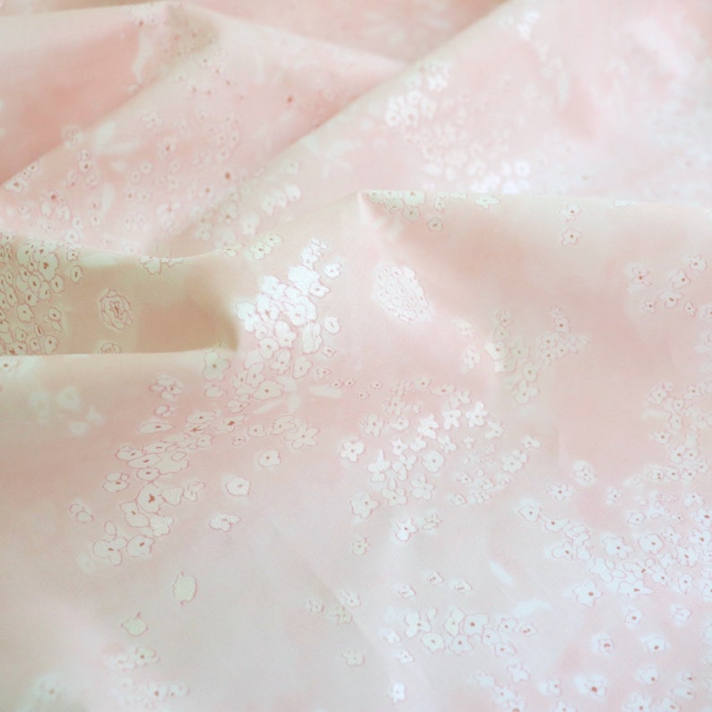 Pode incluir: Um close-up de um tecido rosa com um delicado padr&atilde;o floral. O tecido &eacute; macio e fluido, com flores brancas espalhadas pela superf&iacute;cie. O efeito geral &eacute; leve e arejado, sugerindo um t&ecirc;xtil delicado.