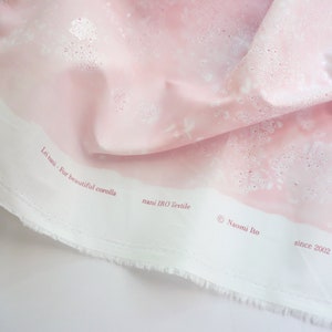 Pode incluir: Tecido rosa claro com um padr&atilde;o floral e o texto "Lei nani - For beautiful corolla" e "nani IRO Textile". O tecido tem um tom rosa suave com detalhes brancos e uma borda branca. O texto "&copy; Naomi Ito since 2002" tamb&eacute;m &eacute; vis&iacute;vel.