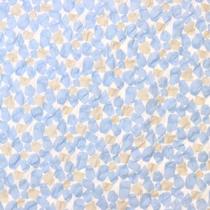 May include: A white fabric with a repeating pattern of blue and tan irregular shapes. The shapes are scattered across the surface, creating a textured appearance. The fabric has a soft, crumpled look.