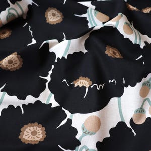 May include: Close-up of a fabric with a floral pattern. Large black flowers with brown centers and white accents are scattered across a white background. Light green stems and seed pods add to the design. The fabric is slightly wrinkled.