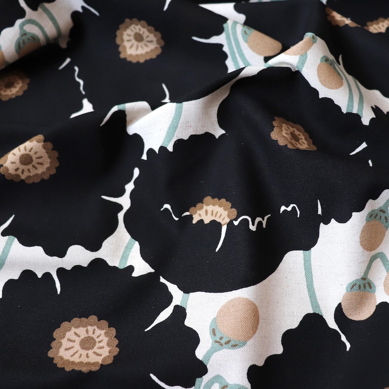 May include: Close-up of a fabric with a floral pattern. Large black flowers with brown centers and white accents are scattered across a white background. Light green stems and seed pods add to the design. The fabric is slightly wrinkled.