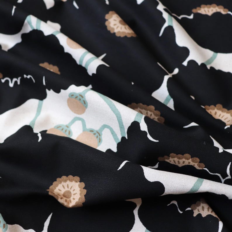 May include: Close-up of a fabric with a floral pattern. The design features large black flowers with white and tan accents. Light blue stems and tan seed pods are also visible. The fabric is folded, creating shadows and texture.