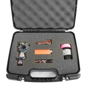 May include: A black hard-shell case with a foam interior for storing smoking accessories. The case contains a glass pipe, a lighter, a small glass jar with a pink lid, and a glass pipe with a colorful design.