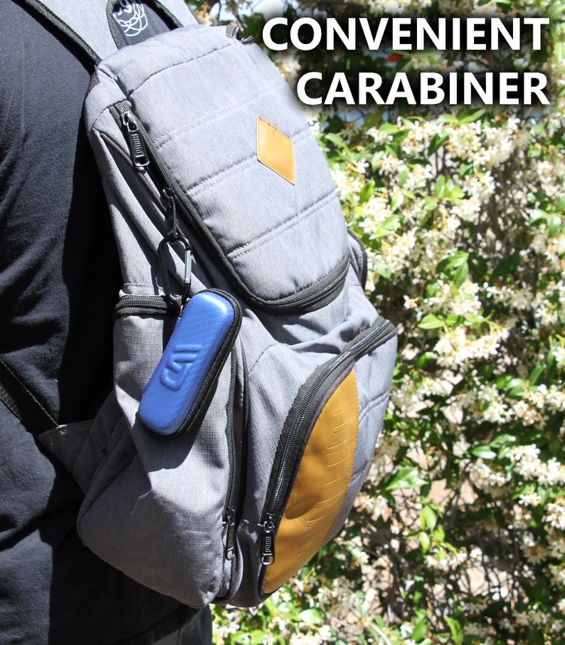 K&ouml;nnte beinhalten: Ein grauer Rucksack mit einem braunen Lederflicken und einem blauen Karabiner, der am Rei&szlig;verschluss befestigt ist. Der Text "CONVENIENT CARABINER" ist in wei&szlig;en Buchstaben auf schwarzem Hintergrund geschrieben.
