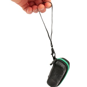 K&ouml;nnte beinhalten: Ein schwarzes und gr&uuml;nes Rei&szlig;verschluss-Etui mit einem schwarzen Band. Das Etui h&auml;ngt an einer Hand.