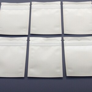 May include: Ten white resealable plastic bags with a zipper closure. The bags are arranged in two rows of five on a gray surface.