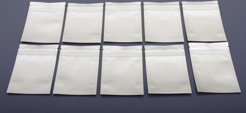 May include: Ten white resealable plastic bags with a zipper closure. The bags are arranged in two rows of five on a gray surface.