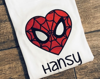 Op de afbeelding: Wit T-shirt met een rood hartvormig Spiderman-ontwerp en de naam "Hansy" eronder geborduurd in het zwart.