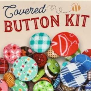 May include: A Covered Button Kit box displaying an assortment of fabric-covered buttons in various colours and patterns, including plaid and floral designs. The box features the text "Covered BUTTON KIT".