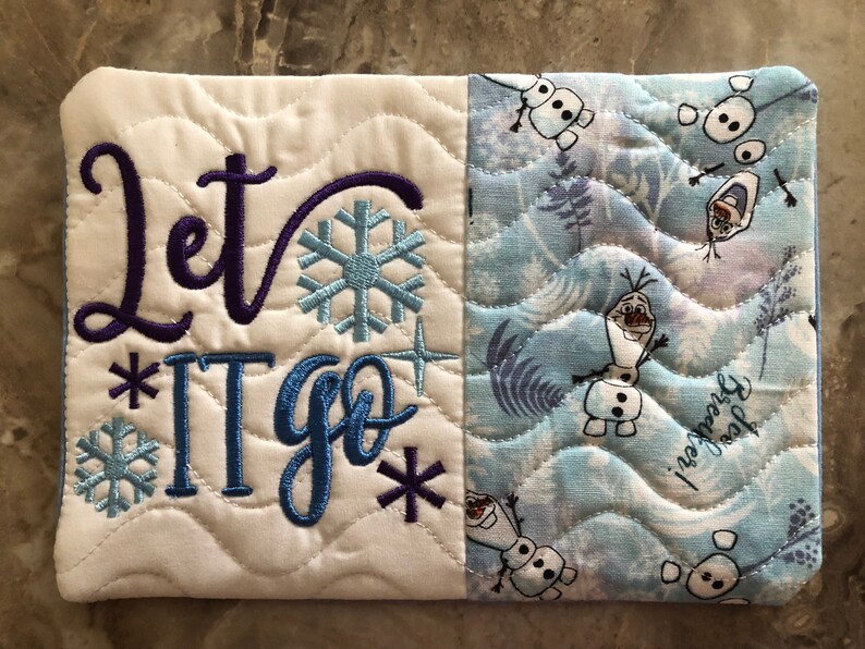 K&ouml;nnte beinhalten: Gestepptes Stoffst&uuml;ck mit dem in Lila und Blau gestickten Schriftzug "Let It Go", zusammen mit Schneeflocken- und Sterndesigns. Die rechte Seite zeigt ein blau-wei&szlig;es Muster mit Olaf dem Schneemann.