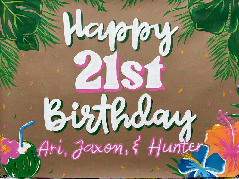 May include: A hand-painted sign on brown paper with the words "Happy 21st Birthday" in white with pink accents. Tropical flowers and leaves frame the text, with names below. A coconut drink is on the left.