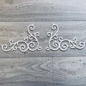 May include: Two white decorative corner pieces with a scroll design. The pieces are made of wood and have a white finish.