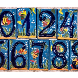 May include: Set of ten ceramic house numbers with a blue background and colorful fish designs. The numbers are 0, 1, 2, 3, 4, 5, 6, 7, 8, and 9.
