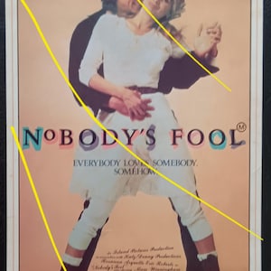 May include: A vintage movie poster for "Nobody's Fool" featuring Rosanna Arquette and Eric Roberts. The poster has a peach background with the film's title in large, colorful letters. The actors are embracing, with the film's title and credits below.