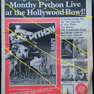 May include: A vintage advert for the "Monty Python Live at the Hollywood Bowl" video. The poster features a black and white illustration of a man with a hat and a long tube. The text includes the names of the performers and other Monty Python films.