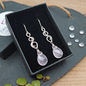 May include: A pair of silver earrings with pink rose quartz drops. The earrings feature a delicate, swirling design.