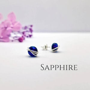 May include: A pair of silver wire wrapped earrings with dark blue glass beads. The earrings are labeled "SAPPHIRE".