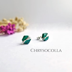 May include: A pair of silver wire wrapped earrings with green chrysocolla stones. The earrings are on a white surface with the word "CHRYSOCOLLLA" written below them.