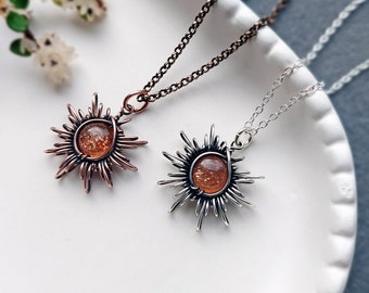 May include: Two sun pendant necklaces with orange sunstone gems. One necklace has a copper chain and the other has a silver chain.